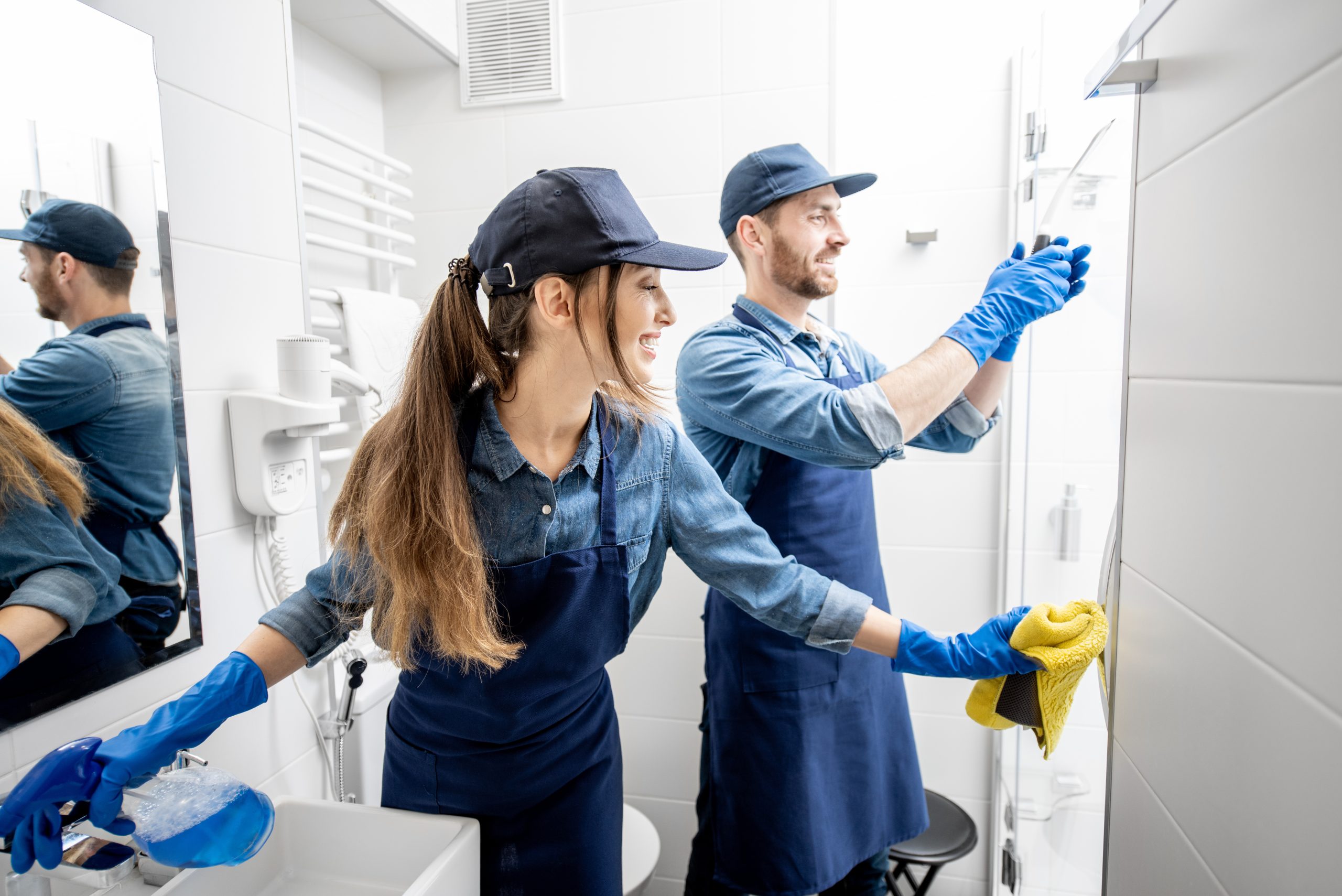 Couple as a professional cleaners in blue uniform cleaning bathroom. Cleaning service concept