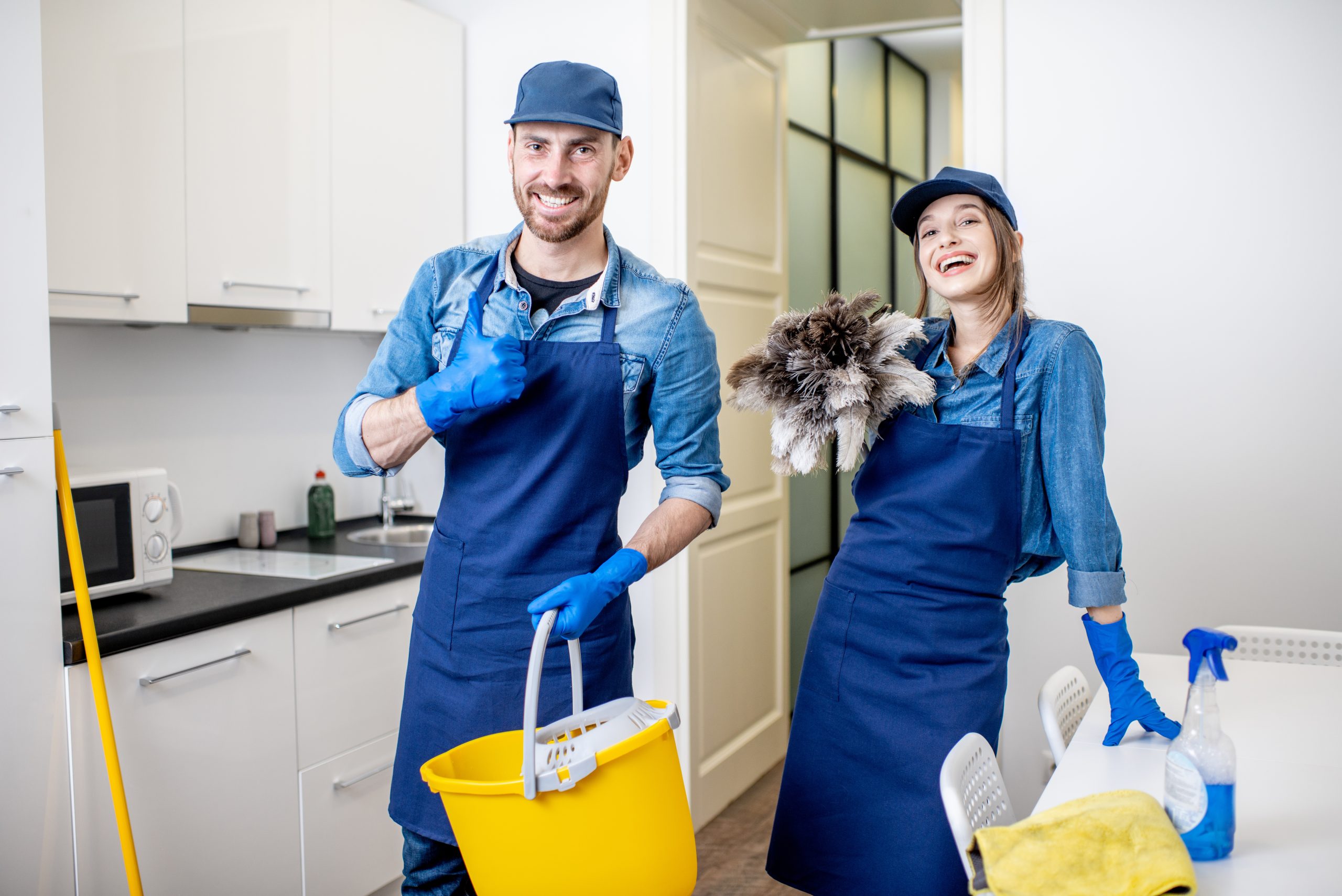 Portrait of a couple as a professional cleaners in uniform standing together with cleaning tools indoors